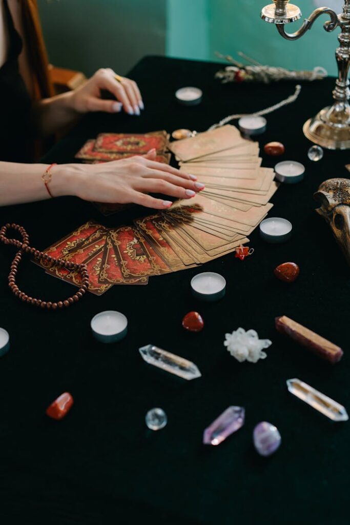 High angle of crop anonymous female fortune teller with tarot cards and stones with candles during divination process